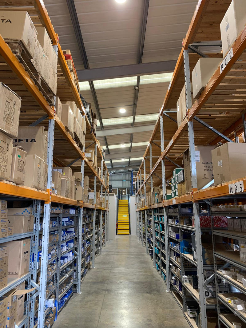 Warehouse interior with shelves stocked with boxes and a staircase in the background.